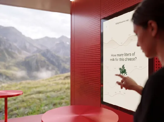 A visitor answers a question on the large touchscreen inside a red pavilion: how many litres of milk for this cheese?
